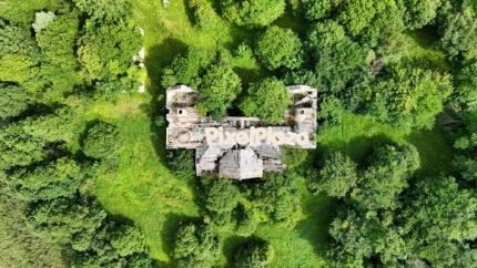 Drone view of a ruined manor in the middle of a lush green forest